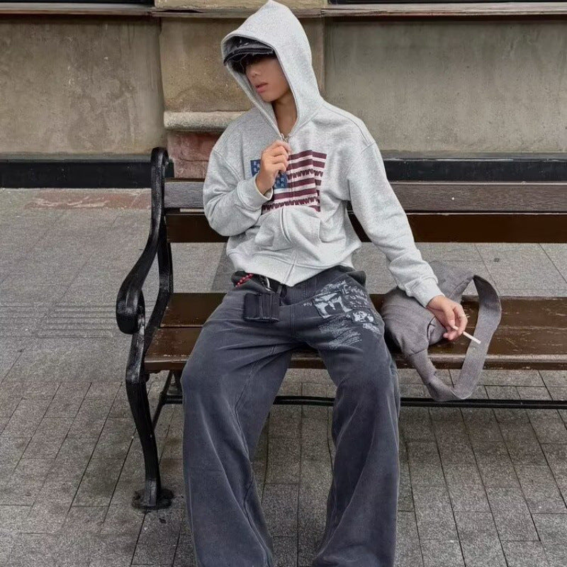 Gray zip up hooded sweatshirt with the letter flag chest print seen while seated on a bench