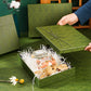 Hand lifting the lid off an open gift box filled with white paper shred beside a candle jar, soap bar and plush toy