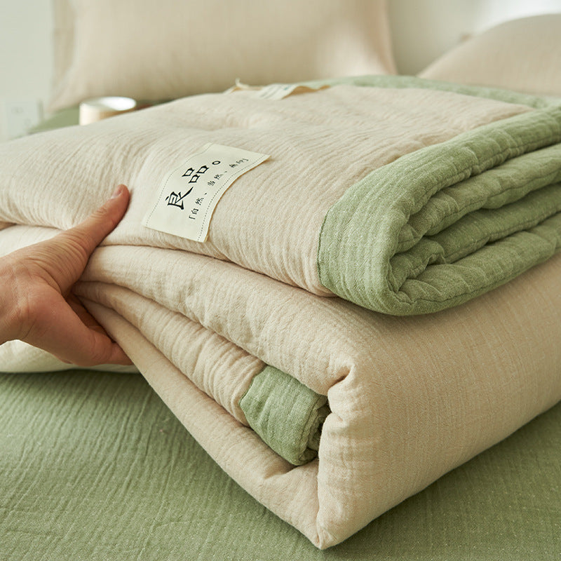 White and green reversible gauze summer quilt laid across a bed
