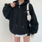 Black oversized hooded sweatshirt with drawstrings and a front pouch pocket, worn with a white shoulder bag