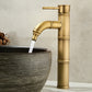 Antique copper bamboo faucet with a curved spout pouring water into a ribbed stone vessel bowl