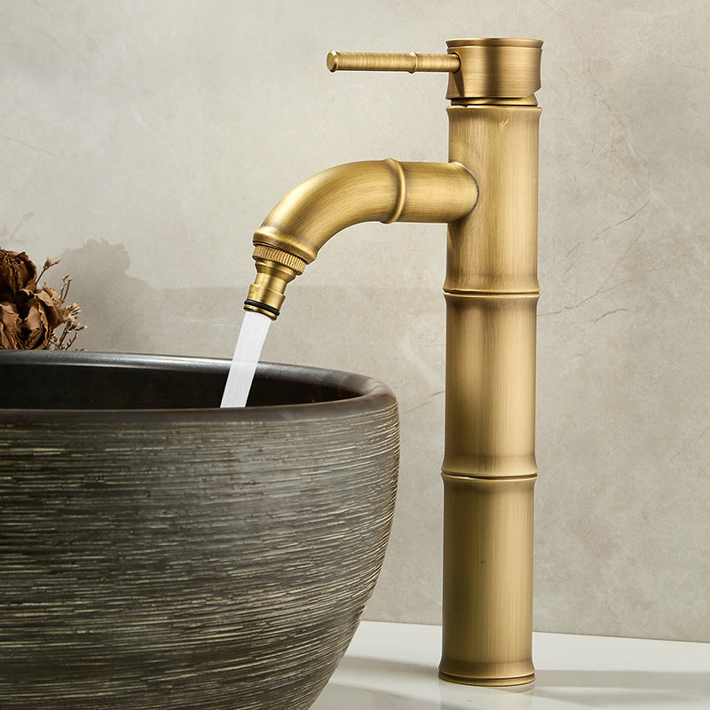 Antique copper bamboo faucet with a curved spout pouring water into a ribbed stone vessel bowl