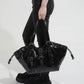 Woman carrying a glossy black hobo shoulder bag with buckle straps, metal grommets and side drawstring cords