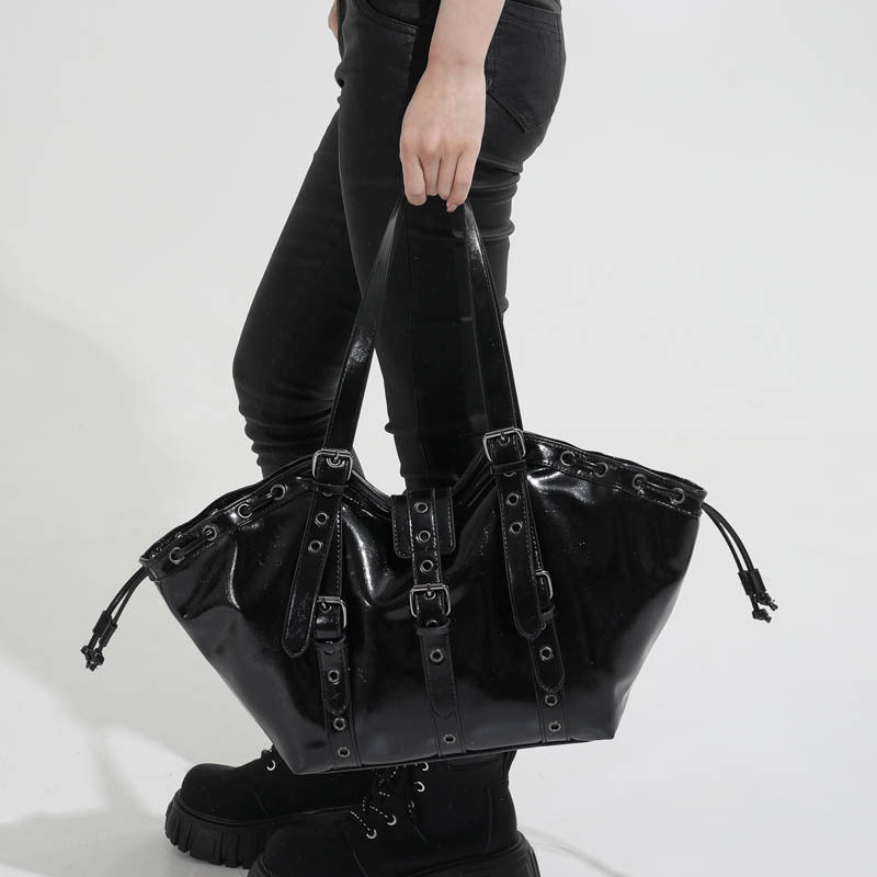 Woman carrying a glossy black hobo shoulder bag with buckle straps, metal grommets and side drawstring cords