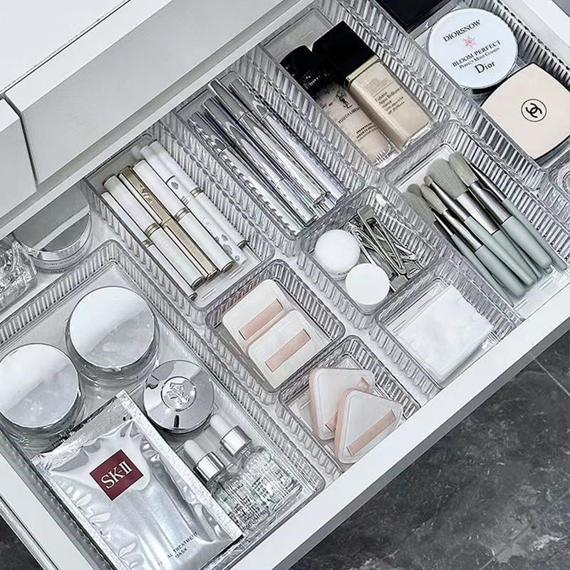 Several clear ribbed trays dividing a drawer of makeup, brushes and skincare