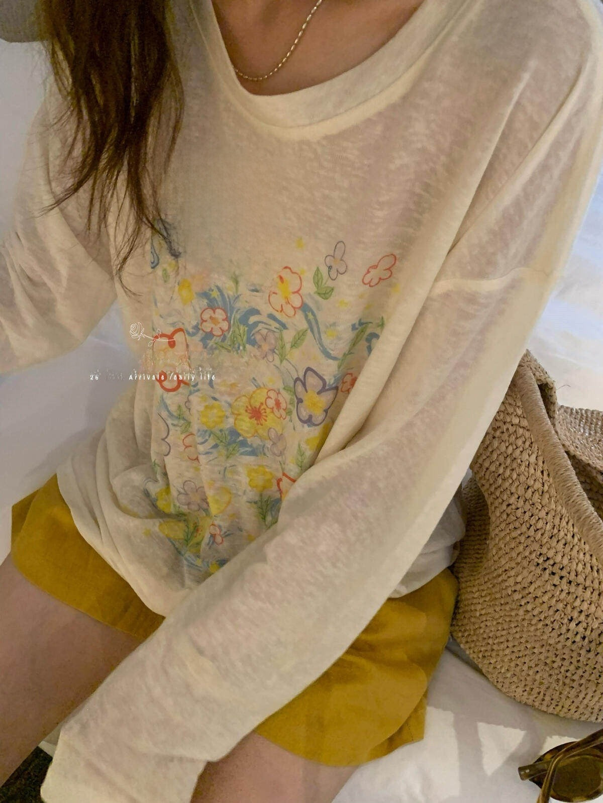 Seated woman in loose ivory floral cotton tee showing airy sheer knit and sleeves