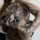 Woman holding a snake print shoulder bag under her arm over a sequin top, gold ball studs visible