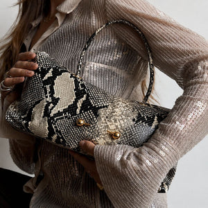 Woman holding a snake print shoulder bag under her arm over a sequin top, gold ball studs visible