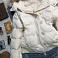 Close view of the white quilted jacket front with stand collar, horn buttons and a ribbed hem