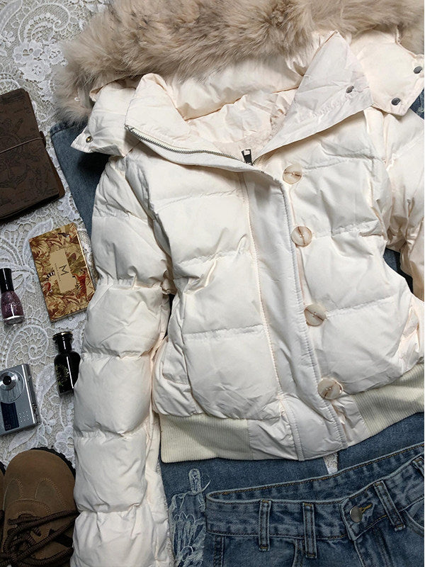 Close view of the white quilted jacket front with stand collar, horn buttons and a ribbed hem