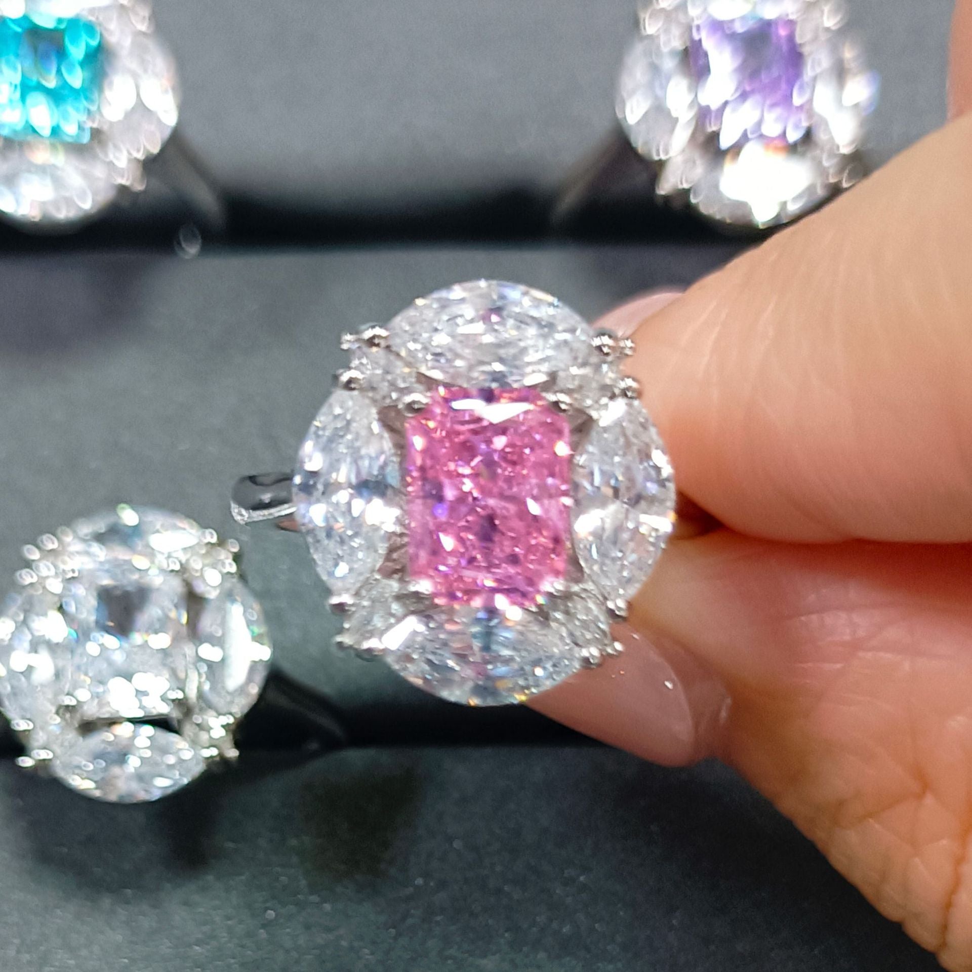 Close up of a pink radiant cut simulated diamond stone ring framed by clear marquise accent stones on a fingertip