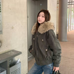 Woman in a dark gray green hooded bomber jacket with vegan fur collar and metal snap details by a concrete wall