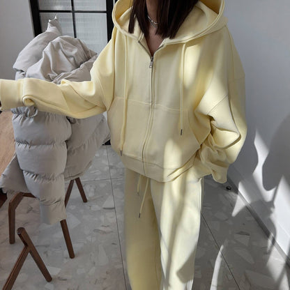 Woman in a light yellow zip-up hoodie and matching trousers holding a puffer coat, close front view