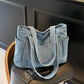 Cowboy light blue denim shoulder tote on a chair, showing the front patch pocket and twin carry straps