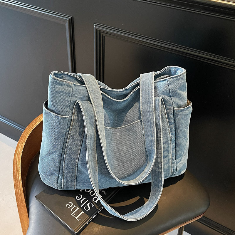 Cowboy light blue denim shoulder tote on a chair, showing the front patch pocket and twin carry straps
