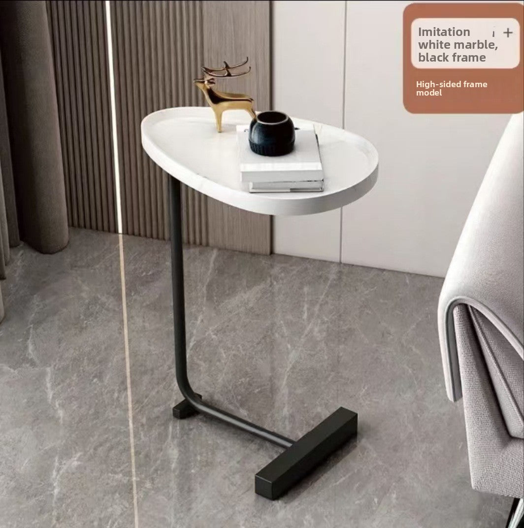 White marble look oval top on a black framed C shaped side table on a grey stone floor