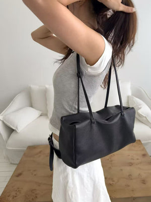 Black soft cowhide shoulder bag with two slim straps worn on one shoulder, side view on a model