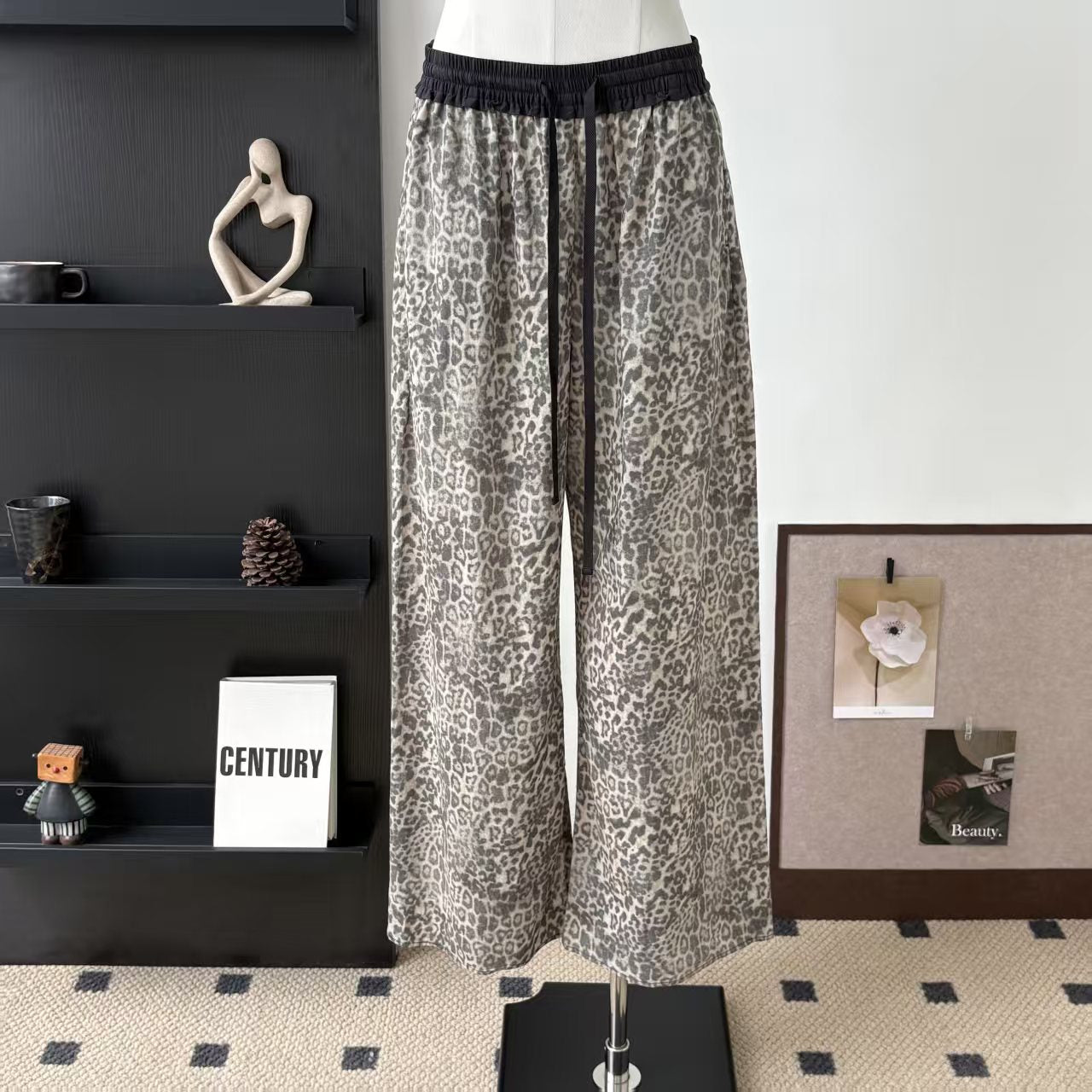 Grey leopard print straight-leg pants with black elastic drawstring waist on display form