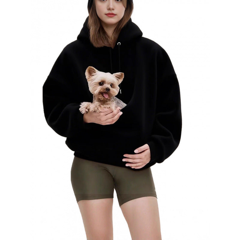 Woman in a black plush hooded sweatshirt holding a small dog in the diagonal front pouch pocket