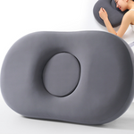 Dark gray oval memory foam pillow with round center hole shown beside a person resting