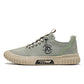 Green lace up canvas sneaker side view on white with a round printed emblem and a beige ribbed sole