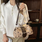 Woman in a white sweater carrying the beige polka dot shoulder bag with brown buckle band on the shoulder