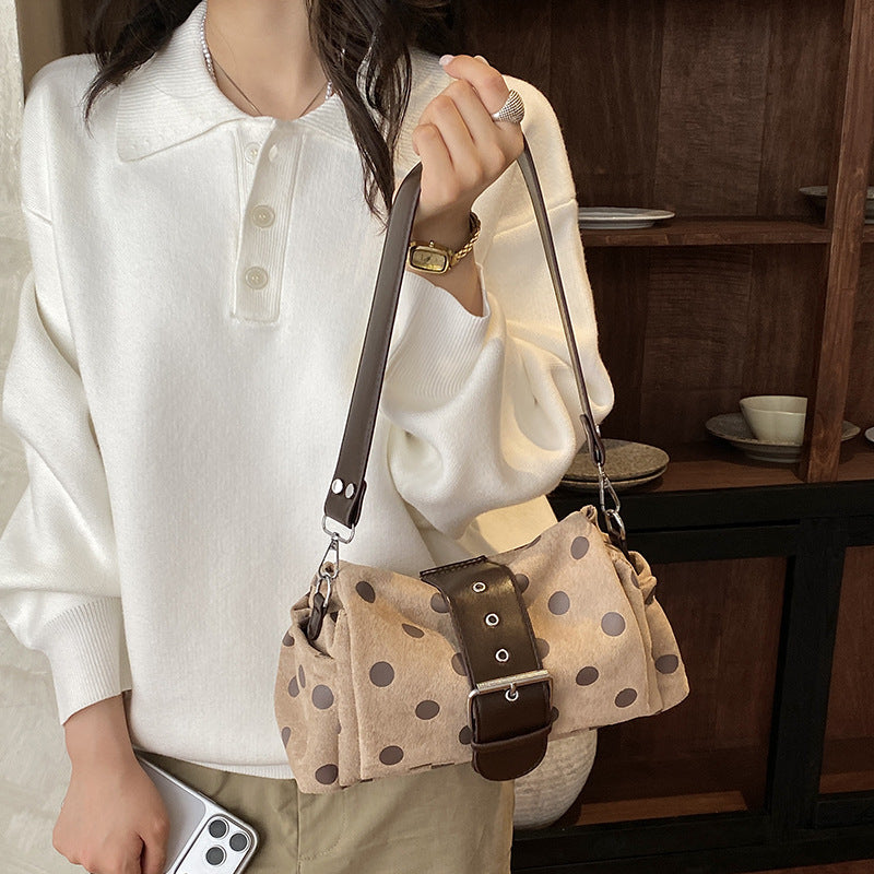 Woman in a white sweater carrying the beige polka dot shoulder bag with brown buckle band on the shoulder