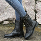 Black lace-up mid-calf boots with side zip and buckle strap worn with jeans on a stone path