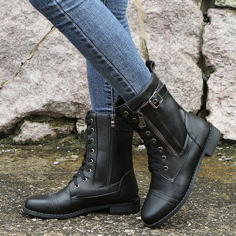 Black lace-up mid-calf boots with side zip and buckle strap worn with jeans on a stone path