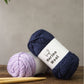Stacked balls of merino wool yarn in pink, blue, purple, navy and cream shades