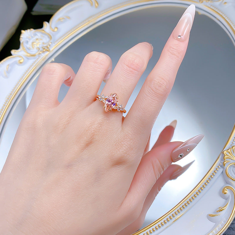 Womens gold toned ring worn on a finger, pink marquise stone running lengthwise in daylight