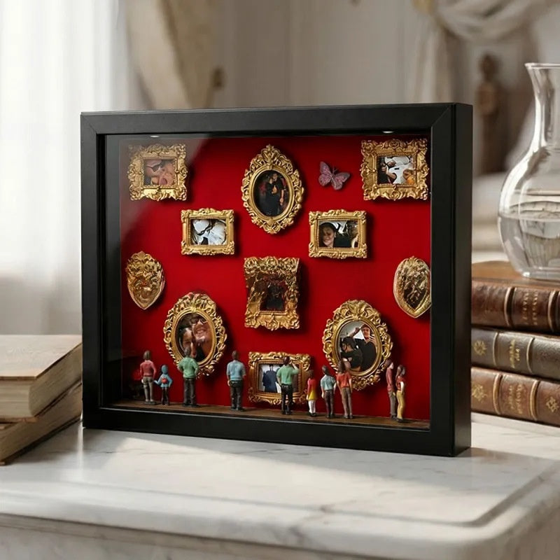 Black shadow box with a red backdrop, gold miniature photo frames, a butterfly and figurines on a marble shelf