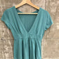 Teal short-sleeve deep V-neck top with an empire waist band and gathered hem on a wooden hanger
