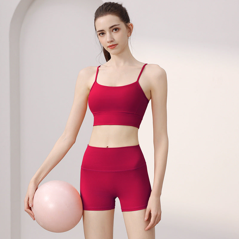 Woman in a raspberry red spaghetti strap sports bra and high-waist shorts set with a pink ball, front view