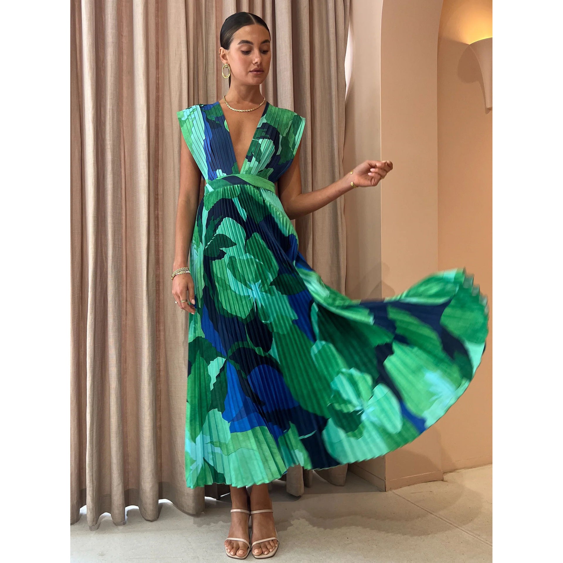 Model twirling the green abstract pleated maxi dress to show the flare