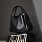 Black leather bucket bag on grey backdrop showing pebbled grain and handle
