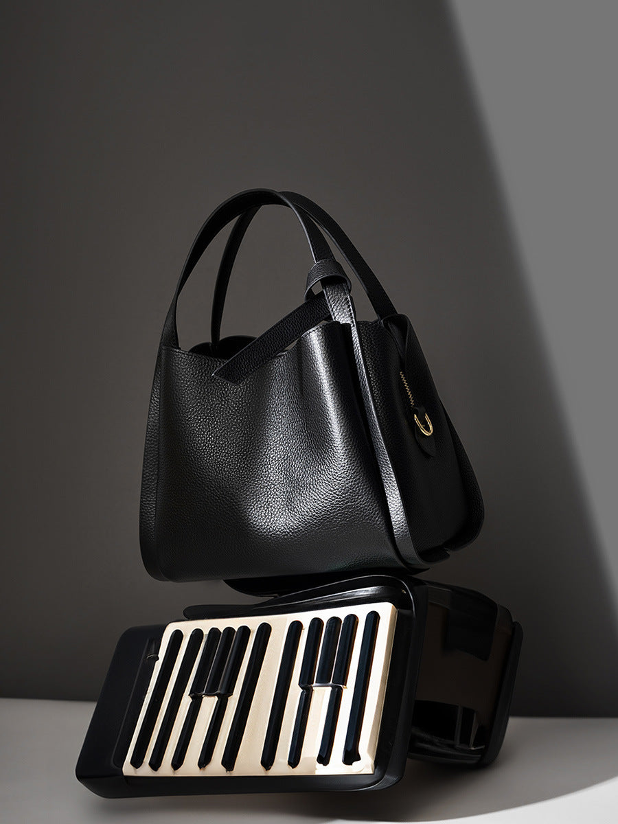 Black leather bucket bag on grey backdrop showing pebbled grain and handle