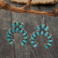 Pair of crescent drop earrings with turquoise colored stones hanging from a branch above dark wood planks