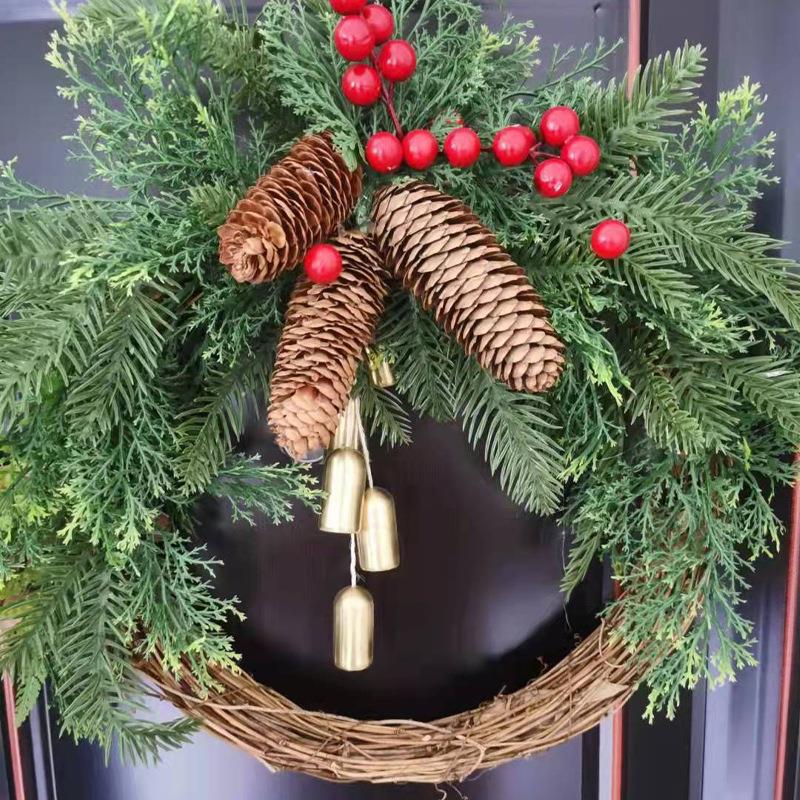 Close view of a Christmas wreath with evergreen sprigs, brown pine cones, red berries and gold-tone bells on a dark door