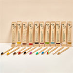 Row of bamboo toothbrushes with colored soft bristles beside kraft paper sleeves