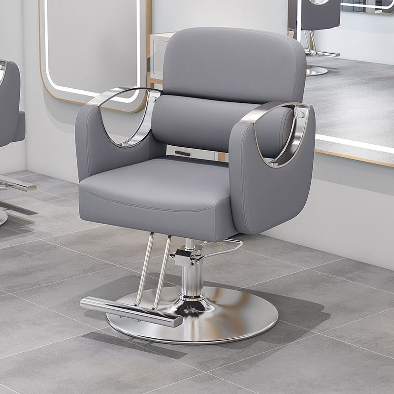 Gray salon styling chair with curved silver armrests on a silver disc base in a salon