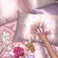 Printed and plain pink and lilac silk pillowcases with scrunchies and a sleep mask on a pink bed