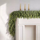 Cedar Christmas garland draped over a white door frame with three gold taper candles set above it