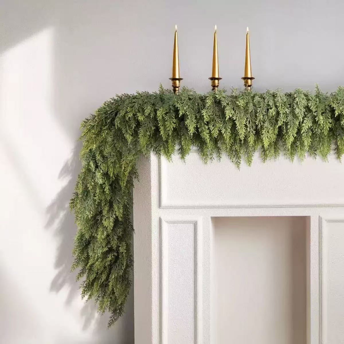 Cedar Christmas garland draped over a white door frame with three gold taper candles set above it