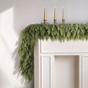 Cedar Christmas garland draped over a white door frame with three gold taper candles set above it