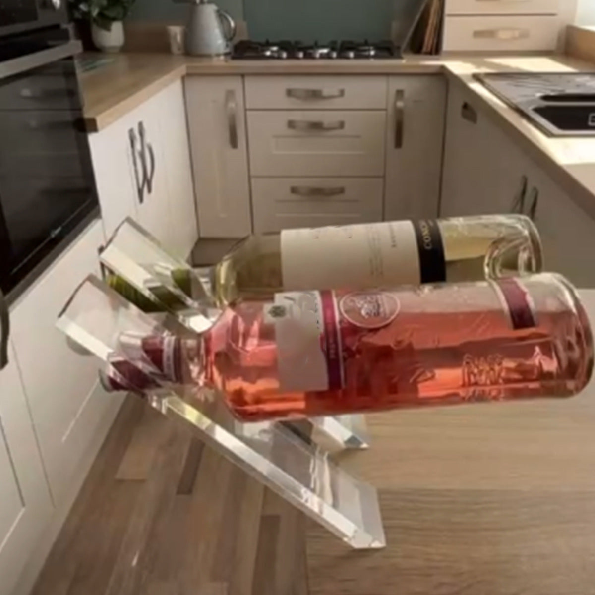Two wine bottles resting at an angle on clear acrylic holders on a kitchen counter