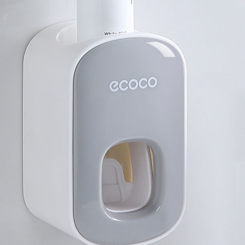 Grey toothpaste dispenser on a bathroom wall with a toothpaste tube standing in the top slot