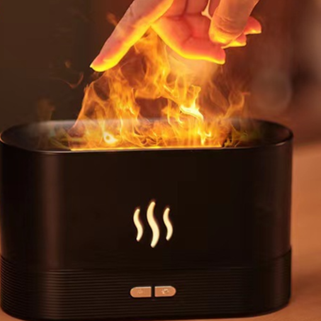 Black flame effect essential oil diffuser releasing an orange lit mist with a hand above it