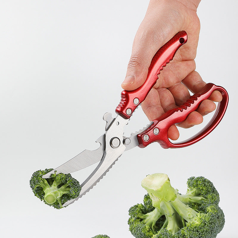 Red handled stainless steel kitchen bone shears cutting broccoli, held in a hand