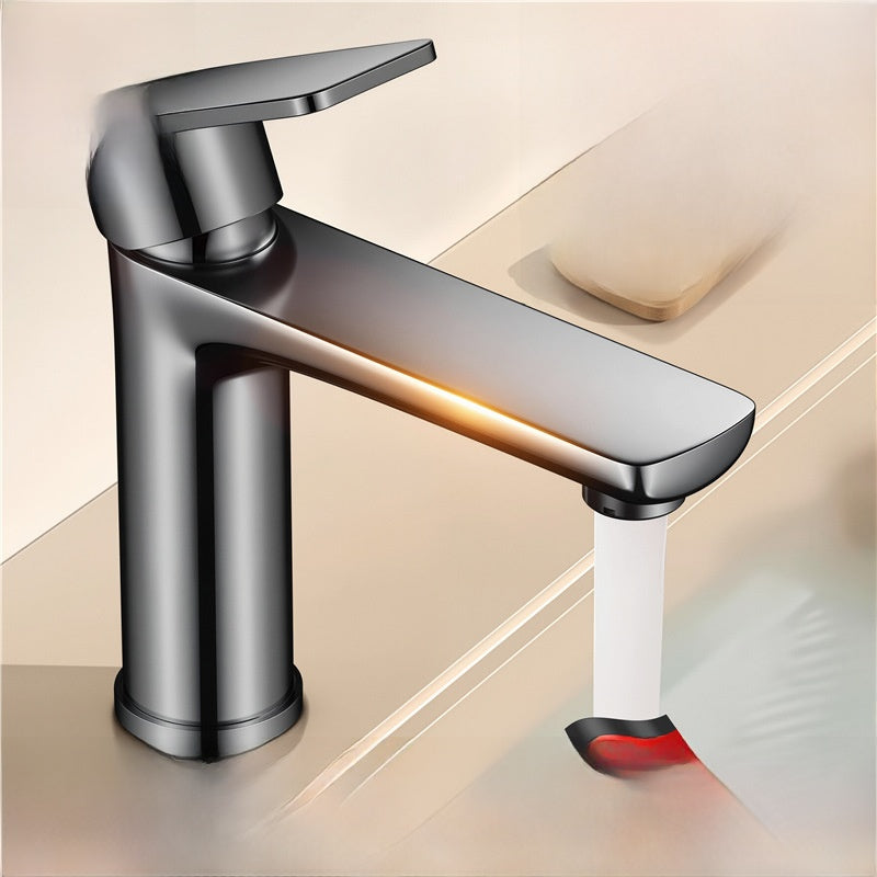Gunmetal gray single lever basin faucet with a glowing orange line along the spout and a stream of water in a bathroom